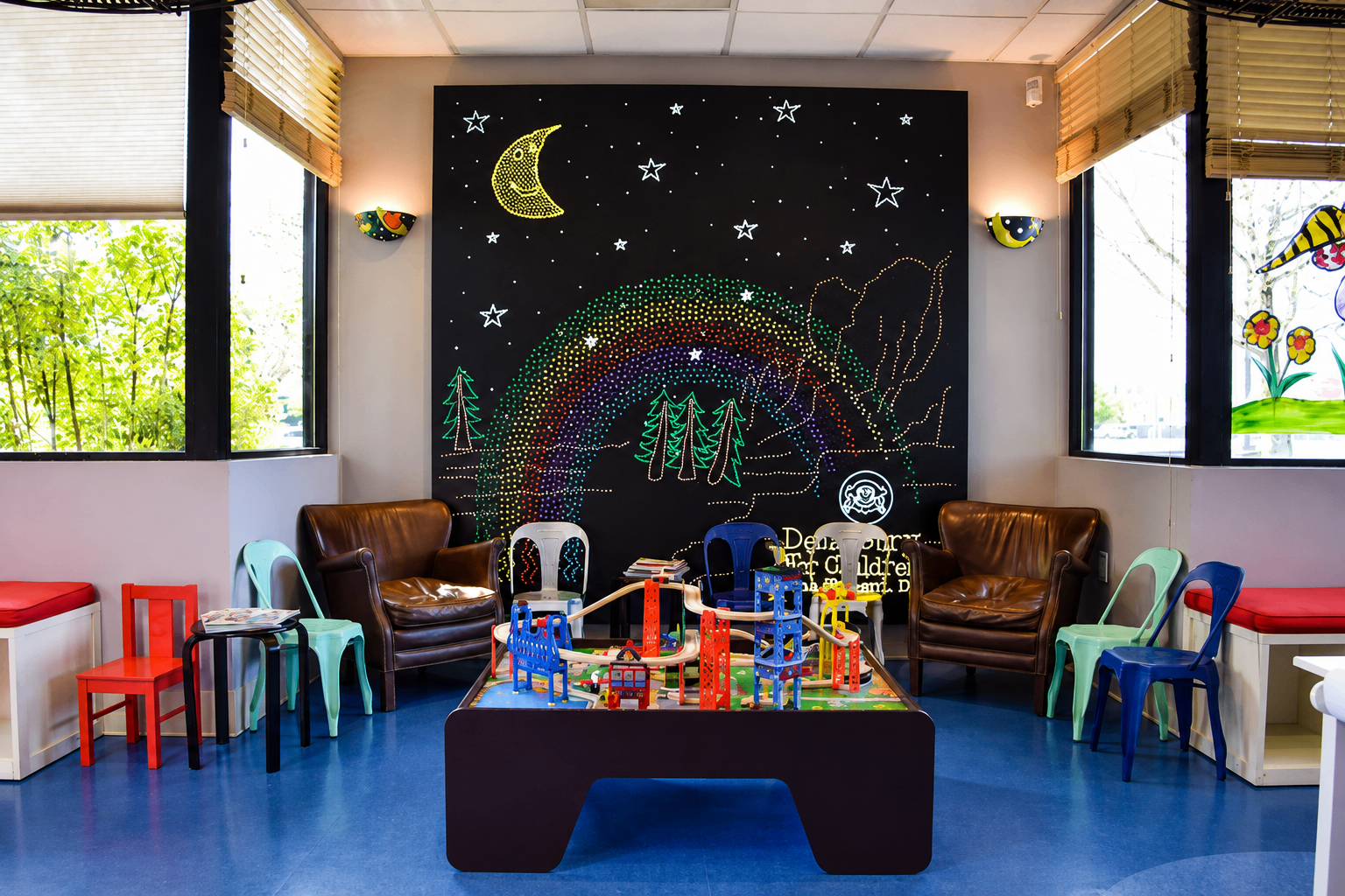 Waiting room with a glowing moon and rainbow mural behind a play table