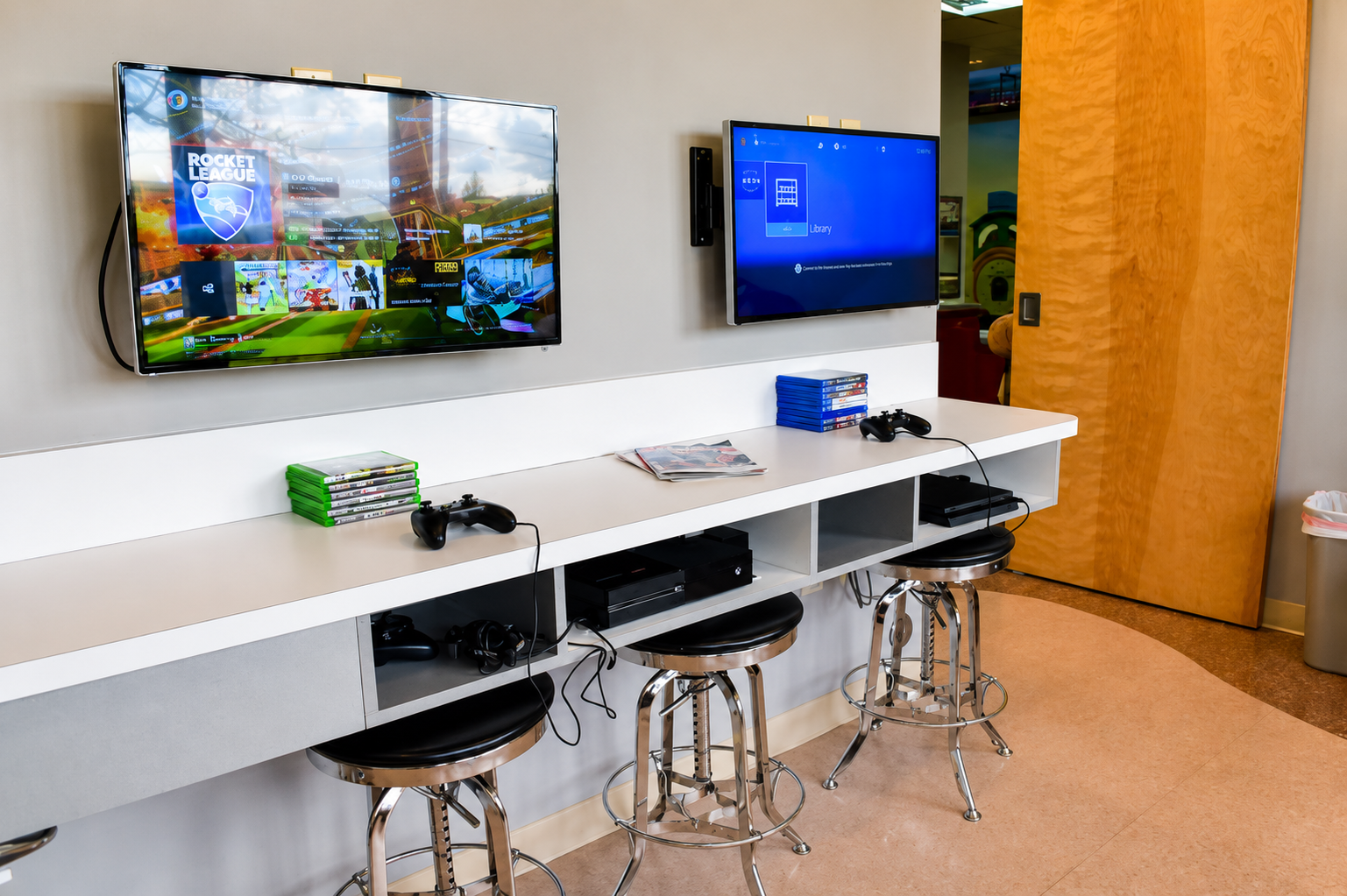 Game station with wall-mounted screens and stools for kids to play while waiting