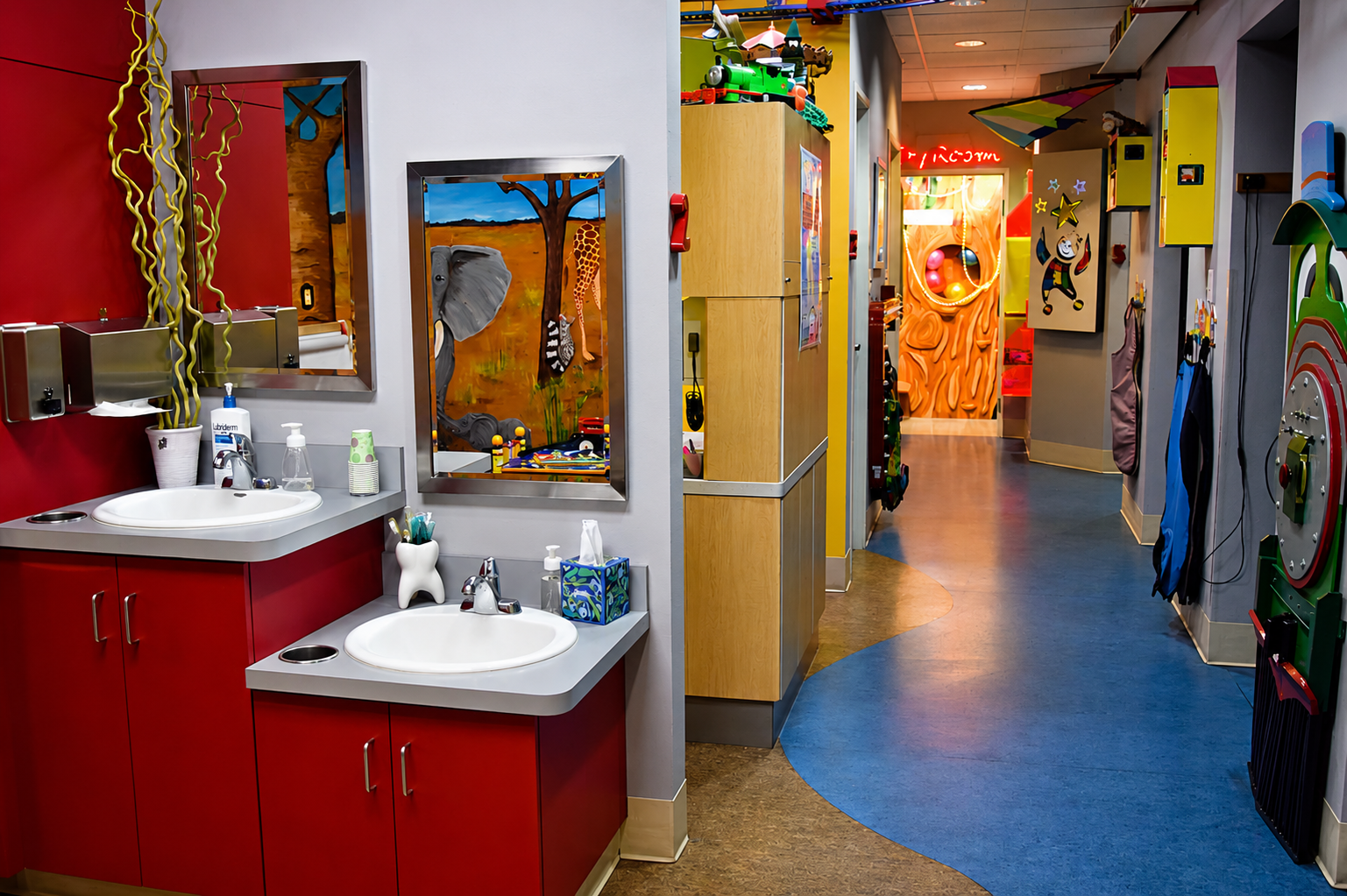 Hallway with red sinks, mirrors, and colorful kids play area visible in the distance